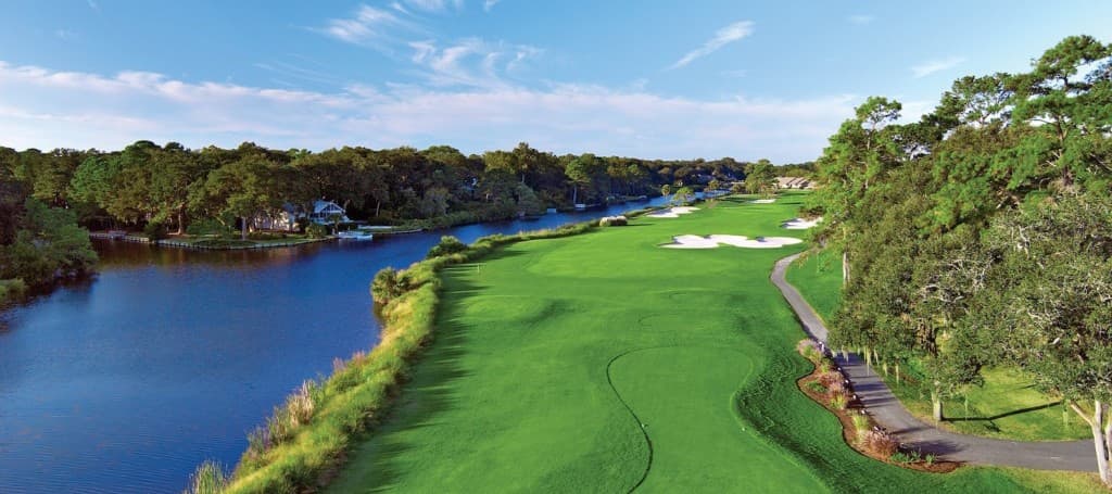 Panoramic aerial view of a Lowcountry golf fairway beside water, bunkers, and tree-lined coast